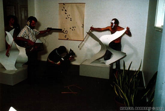 Vernissage de l'expostion Marcel Barbeau à la galerie Esperanza, Montral le 27 novembre 1985. Le percussionniste Vincent Dionne jouant de la sonorité des sculptures sculpture de Barbeau de 1985 dans le cadre d'une improvisation musicale. Maquillage et conception de la performance, Marcel Barbeau. Photo Robert Etchevery pour Marcel Barbeau. © ADAGP- PARIS pour Marcel Barbeau.